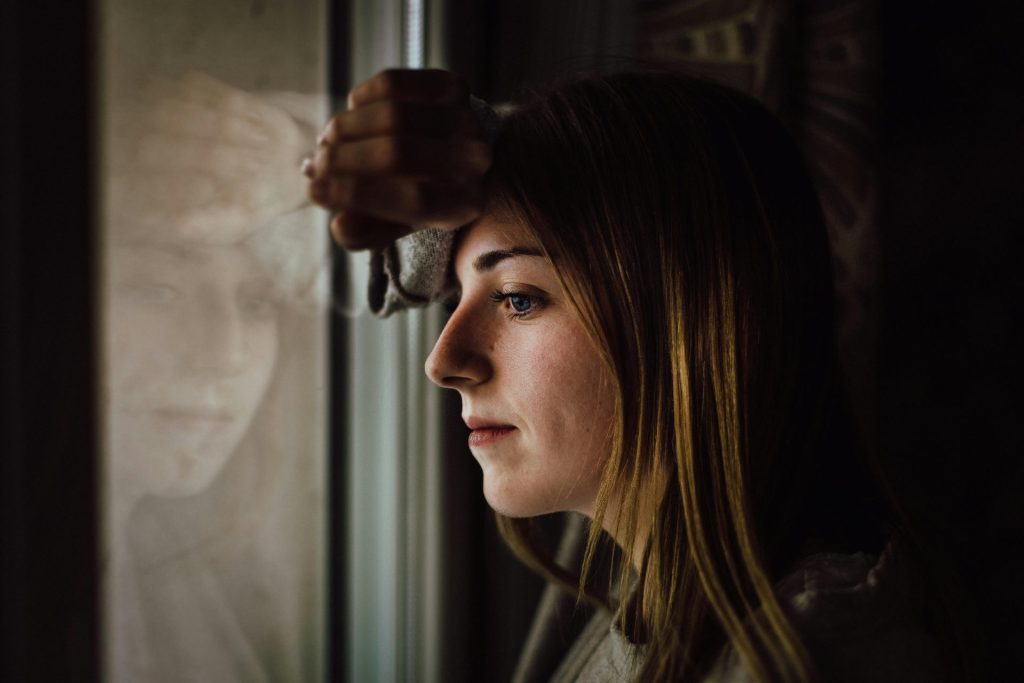 À l'intérieur, une jeune femme contemplative regarde par la fenêtre, l'air pensif.