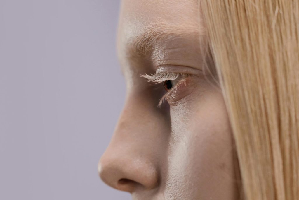 Vue de profil du visage d'une femme blonde, l'accent étant mis sur l'œil et les cils dans un décor minimaliste.