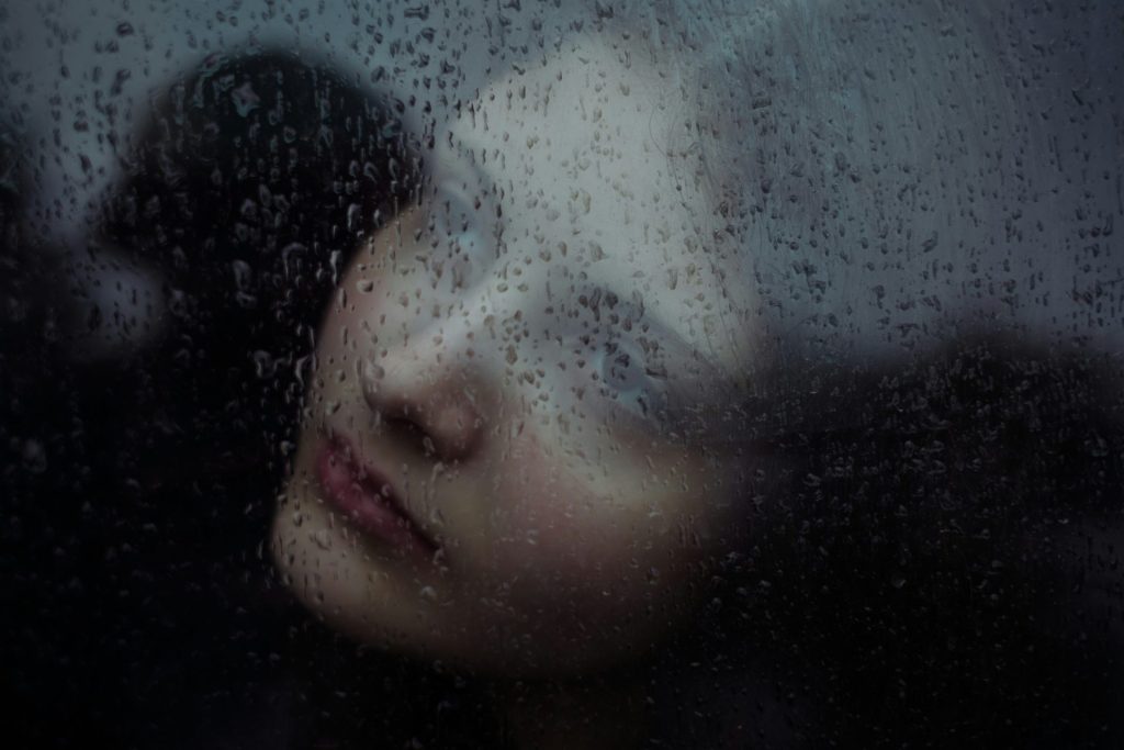 Visage de femme aperçu à travers une vitre striée par la pluie